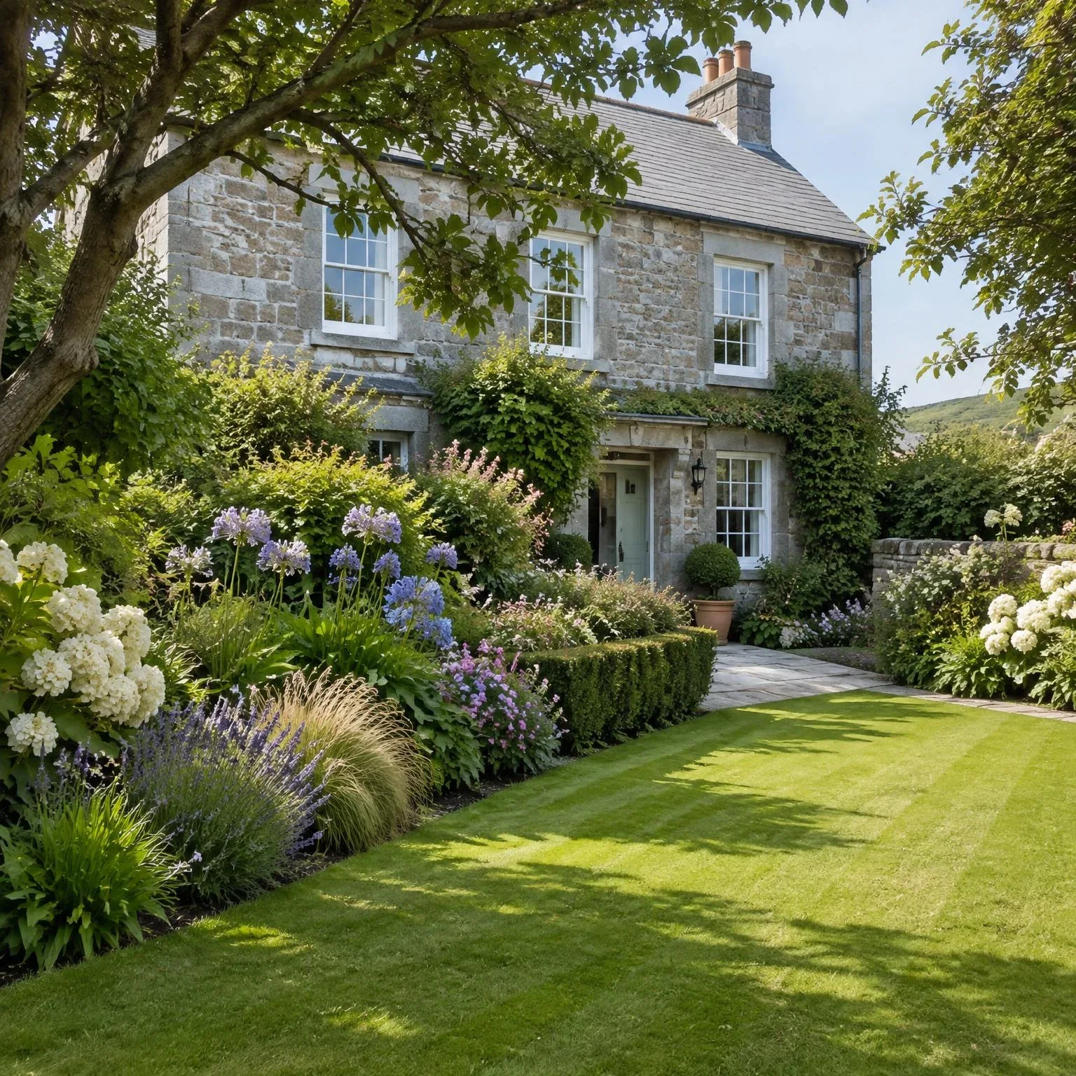 Stone Cornish cottage with a neatly striped lawn, clipped hedges and summer flower borders